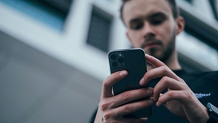 Mann wird aus der Froschperspektive fotografiert und schaut dabei auf sein iPhone