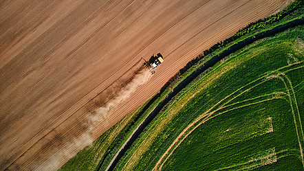 Bild in Vogelperspektive, welches eines Landwirtschaftsfahrzeug das über ein Feld fährt