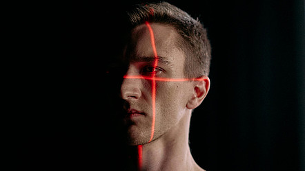 ein Mann schaut in die Leere und wird dabei von einem kreuzförmigen Laserstrahl abgescannt
