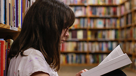 Eine junge Frau in einer Bibliothek liest in einem Fachbuch