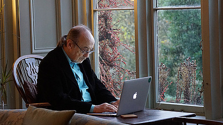 Einer alter Mann mit Brille und schwarzer Jacke arbeitet gerade mit einem Laptop.