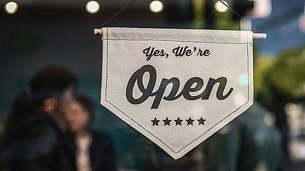 Ein Wimpel vor einem Fenster mit der Aufschrift: Yes, we're open. Darunter fünf Sterne.