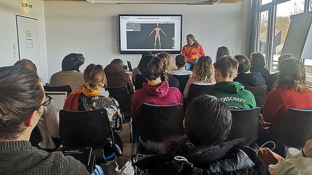 Blick auf eine Vortragenden, Michael Bressler, und sein Publikum. Auf einem Bildschirm ist das Modell eines menschlichen Körpers abgebildet und die Worte "positioning the phantom limb" 