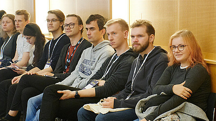 Eine Gruppe junger Studierender, sitzend bei einer Veranstaltung, mehrere von ihnen tragen Badges der INFORMATIK22
