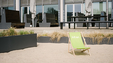 Ein Liegestuhl mit dem Logo der htw steht im Sand auf dem Campus
