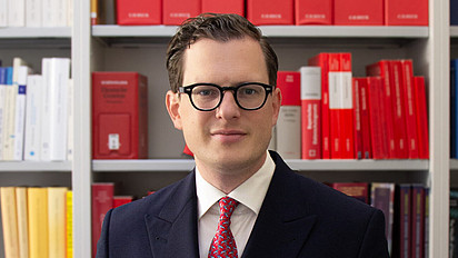 Porträt von Moritz Heinmann im Anzug vor einem Bücherregal mit juristischer Literatur