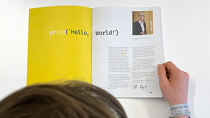 Eine Person blättert im aufgeschlagenen GI-Mitgliedermagazin. Zu sehen ist der Schriftzug: Hello, world!
