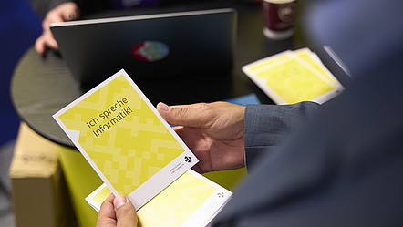 Blick über die Schulter einer Person, die eine Postkarte in der Hand hält, auf der "Ich spreche Informatik" steht.