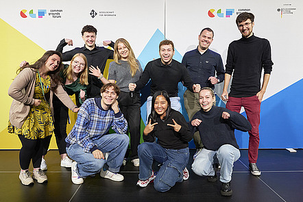 Eine Gruppe junger Menschen posiert vor der Pressewand des Common Grounds Forum