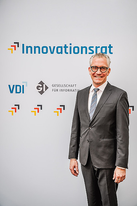 Prof. Dr. Martin Wolf, Präsident der Gesellschaft für Informatik (GI), in Anzug und Krawatte vor einer Pressewand mit den Logos von Innovationsrat, VDI und GI.