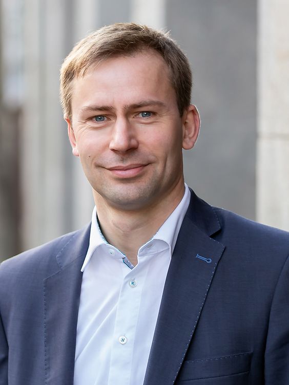 Porträt eines lächelnden Mannes im Anzug vor einem Gebäude