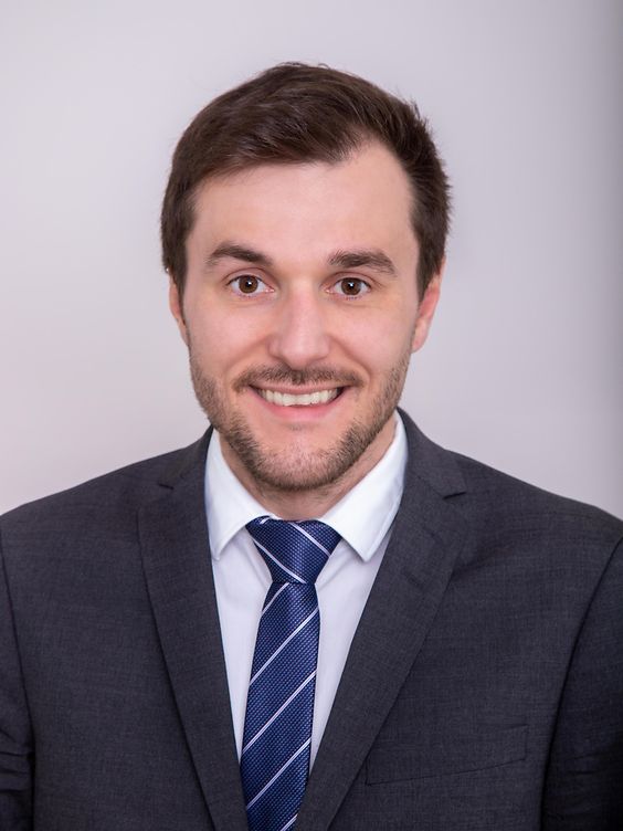 Lächelnder Mann im Anzug mit gestreifter Krawatte vor hellem Hintergrund